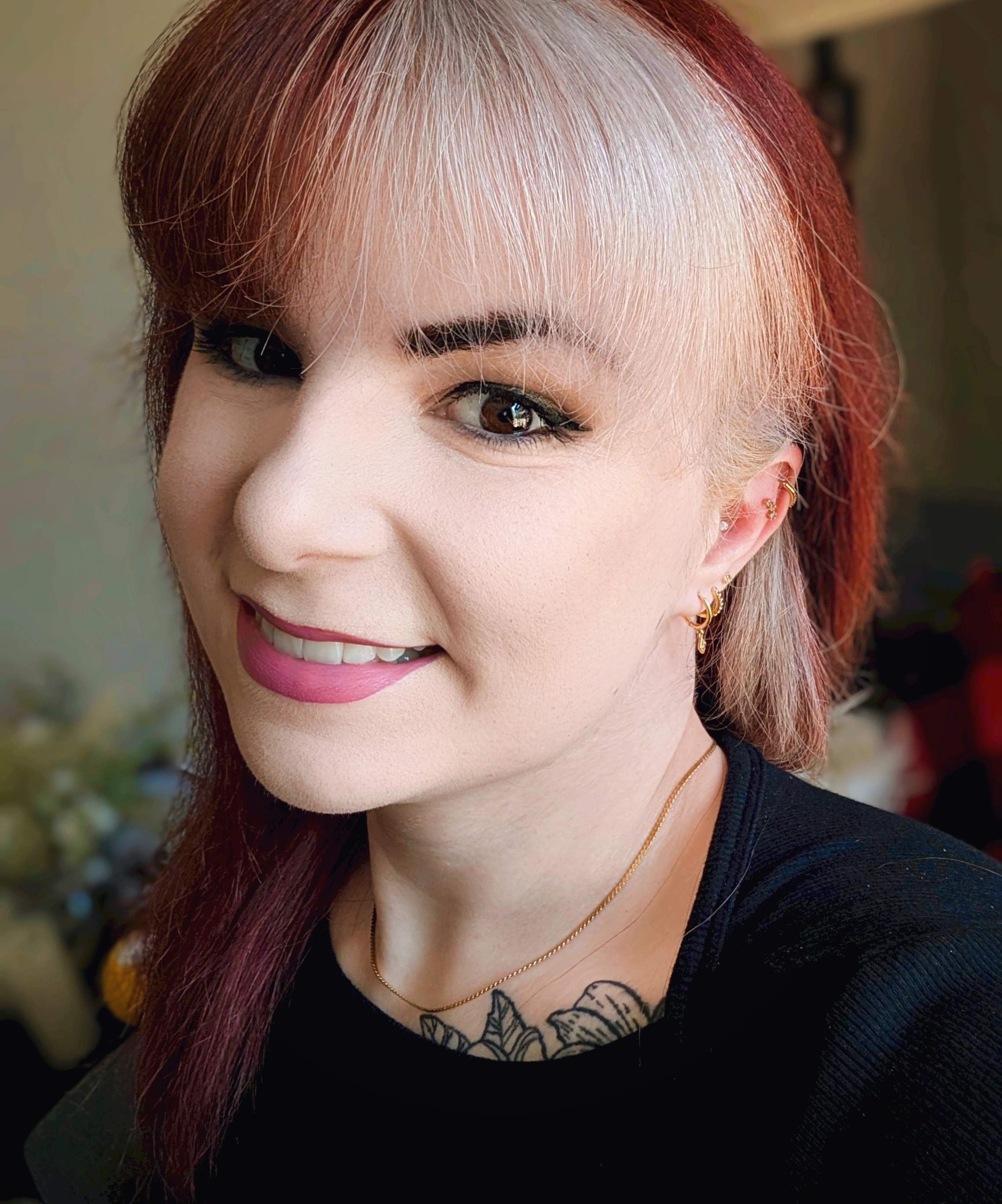 Katerina Rose, smiling, with red and blonde hair, gold jewelry, and a floral tattoo